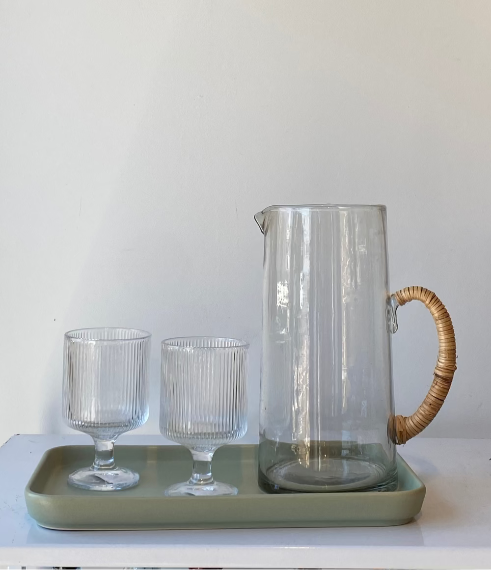 Clear glass pitcher with a wooden handle and two glasses on a green tray against a white background