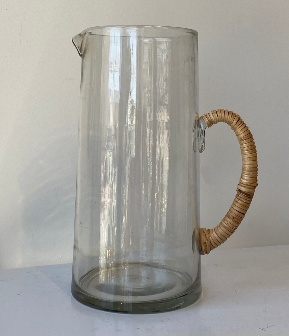 Clear glass pitcher with a wicker handle on a white background